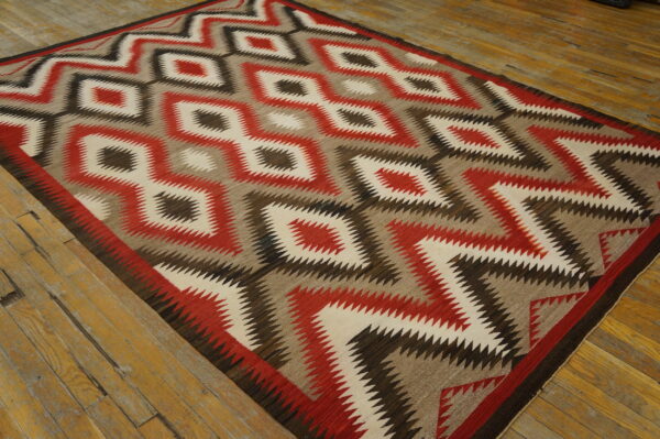 Flatweave rug with red, cream, brown, and taupe zigzag diamond pattern on distressed wood flooring.