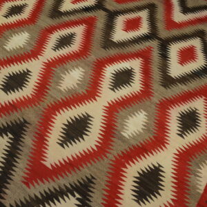 Red, cream, gray, and brown serrated geometric diamond flat weave rug on hardwood flooring.