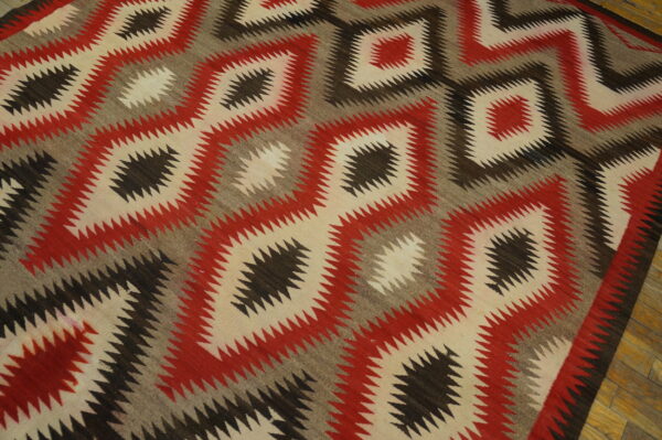 Red, cream, gray, and brown serrated geometric diamond flat weave rug on hardwood flooring.