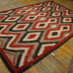 Flat rug featuring red, black, cream, and gray serrated geometric diamond patterns on wood floor.