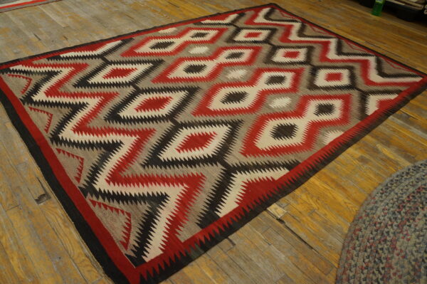 Flat rug featuring red, black, cream, and gray serrated geometric diamond patterns on wood floor.