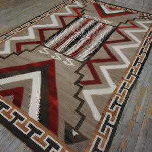 Geometric flat-weave rug in tan, red, white, and dark brown on a distressed wood floor.