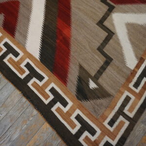 Flatweave rug featuring geometric zigzag patterns in red, brown, white, and taupe on weathered wood floors.