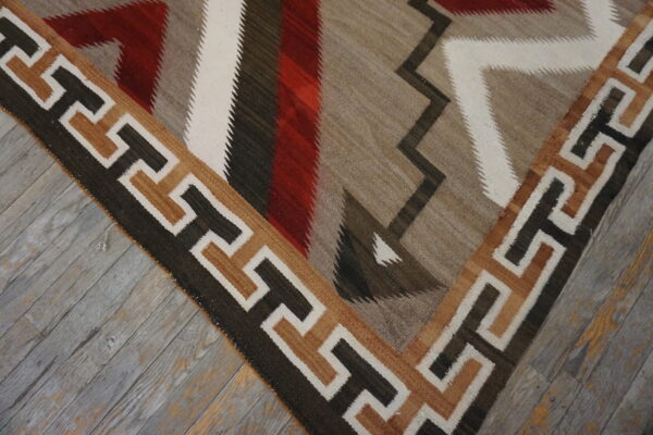 Flatweave rug featuring geometric zigzag patterns in red, brown, white, and taupe on weathered wood floors.
