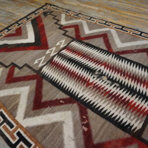 Geometric rug featuring red, white, and black zigzag patterns and a diamond center on rustic wood floor.