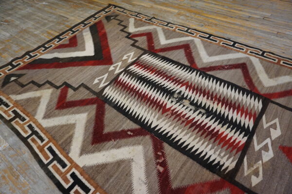Geometric rug featuring red, white, and black zigzag patterns and a diamond center on rustic wood floor.