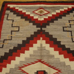 Gray, red, and brown flatweave rug featuring a central stepped pattern on a light wood floor.