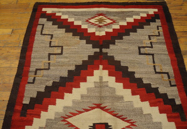Gray, red, and brown flatweave rug featuring a central stepped pattern on a light wood floor.