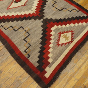 Gray and red flatweave rug with a jagged geometric pattern centered on worn light brown hardwood floors.