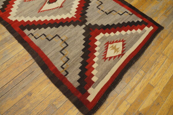 Gray and red flatweave rug with a jagged geometric pattern centered on worn light brown hardwood floors.