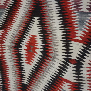 Geometric flatweave rug featuring zig-zagging diamond stripes in black, bright red, gray, and white.