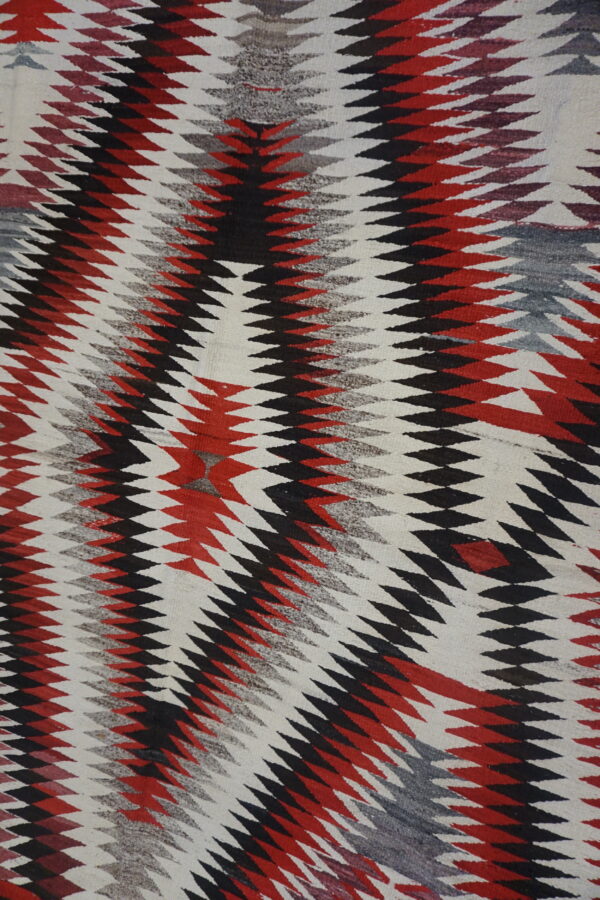 Geometric flatweave rug featuring zig-zagging diamond stripes in black, bright red, gray, and white.
