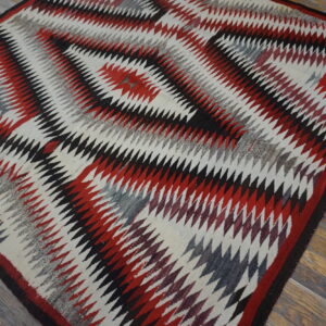 Low-pile rug with red, black, and gray serrated diamond patterns on rustic wood planks.