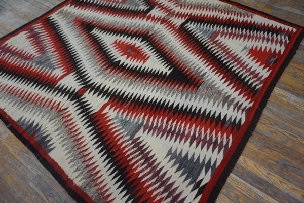 Low-pile rug with red, black, and gray serrated diamond patterns on rustic wood planks.