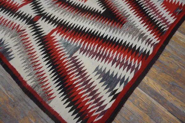 Serrated geometric rug in cream, red, black, and gray on rustic wood plank flooring.