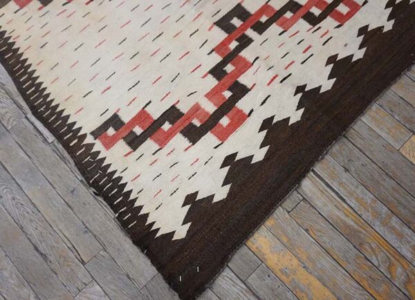 Geometric flatweave rug in cream, brown, and rust colors rests on distressed gray wood flooring.