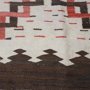 Geometric flat-woven rug detail with white, brown, and red interlocking patterns and a stepped border design.