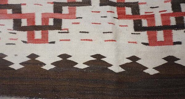 Geometric flat-woven rug detail with white, brown, and red interlocking patterns and a stepped border design.