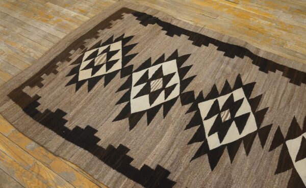 Low-pile brown and cream geometric rug with dark stepped borders lying on distressed hardwood.