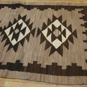 Geometric flatweave rug in natural brown tones with large dark brown and cream diamond designs on wood floor.