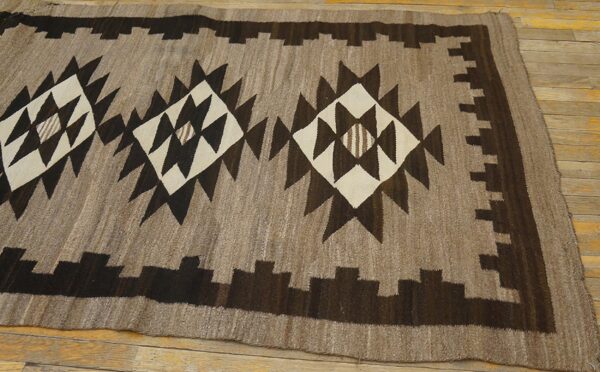 Geometric flatweave rug in natural brown tones with large dark brown and cream diamond designs on wood floor.