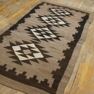 Taupe and dark brown geometric flatweave rug with large diamonds on worn wooden floors.