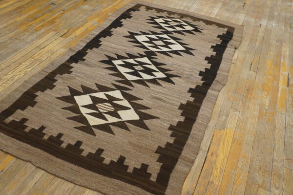 Taupe and dark brown geometric flatweave rug with large diamonds on worn wooden floors.