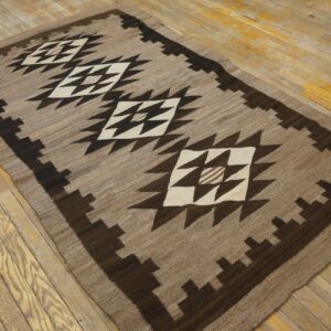 Tan and dark brown geometric rug with white diamonds resting on a distressed wood plank floor.