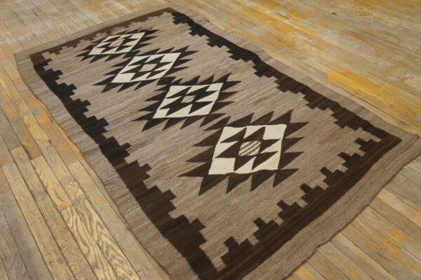 Tan and dark brown geometric rug with white diamonds resting on a distressed wood plank floor.