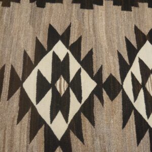Close view of a flatweave rug in brown, cream, and taupe with jagged geometric diamonds.