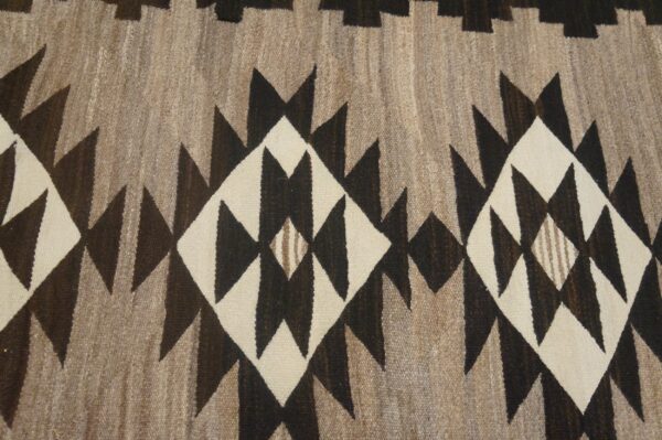 Close view of a flatweave rug in brown, cream, and taupe with jagged geometric diamonds.