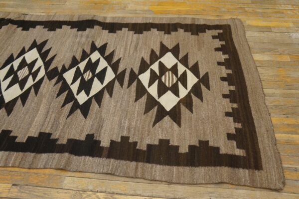 Brown, dark brown, and cream geometric rug featuring large central diamonds laid on a yellow wood floor.