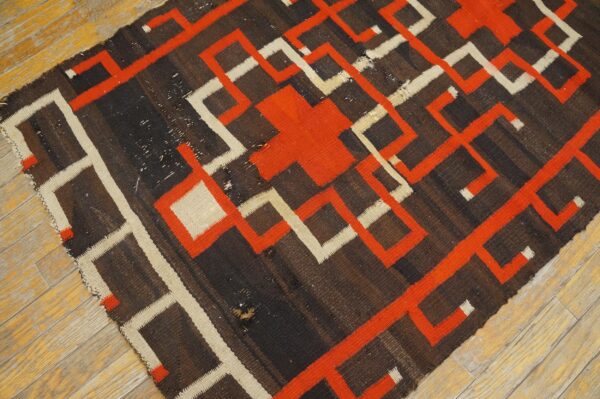 Flat-weave rug with brown, orange, and cream interlocking geometric patterns sits on wood planks.