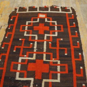Geometric flatweave rug in brown, orange, and off-white rests on worn yellow wood flooring.