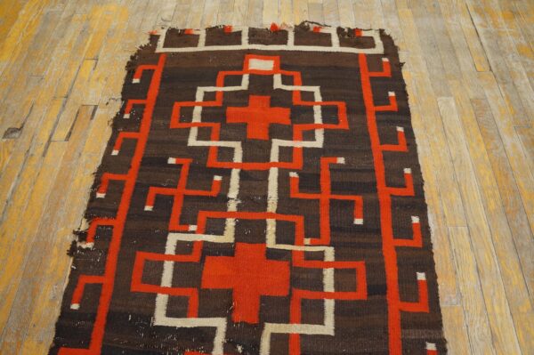 Geometric flatweave rug in brown, orange, and off-white rests on worn yellow wood flooring.