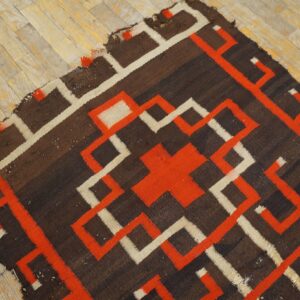 Brown rug with bold orange and cream geometric pattern rests on light-colored wood flooring.