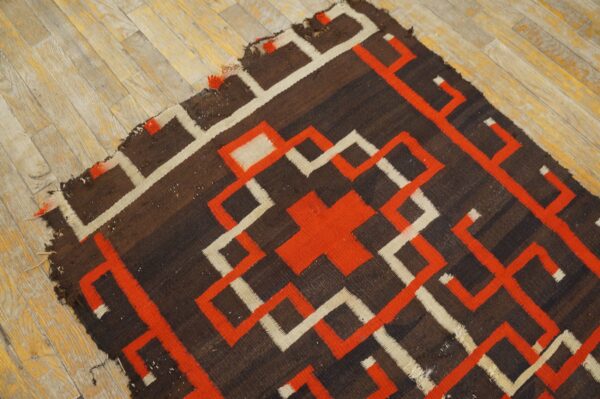 Brown rug with bold orange and cream geometric pattern rests on light-colored wood flooring.