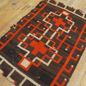 Dark brown flatweave rug featuring interlocking red and cream geometric designs on a distressed wood floor.