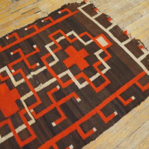 Dark brown flatweave rug with orange and cream geometric patterns rests on distressed wood flooring.