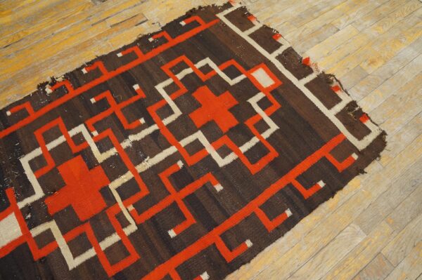 Dark brown flatweave rug with orange and cream geometric patterns rests on distressed wood flooring.
