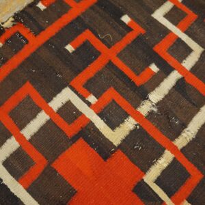 Worn flatweave rug with striking orange, cream, and brown geometric patterns lying on a wood floor.