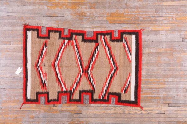 Tan, red, black, and white geometric rug with stepped border and diamonds on distressed hardwood floor.