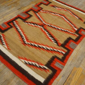 Geometric rug with tan, red, brown, and white serrated patterns rests on worn hardwood flooring.
