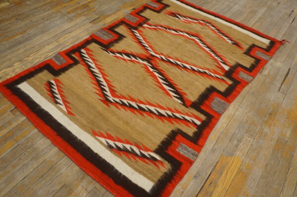 Geometric rug with tan, red, brown, and white serrated patterns rests on worn hardwood flooring.