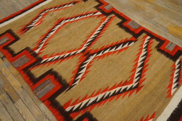 A tan rug with red, black, and white zigzag patterns lies on distressed wood floorboards.