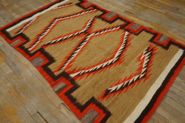 Tan, red, and brown flatwoven rug featuring large jagged geometric diamonds on distressed wood floor.