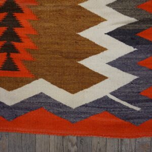 Geometric flatweave rug featuring orange, brown, gray, and cream patterns over weathered wood floors.