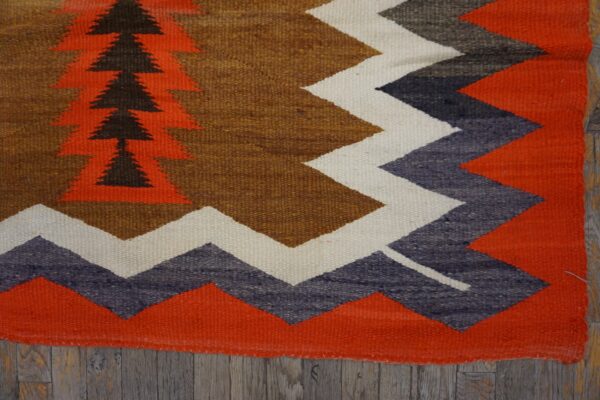 Geometric flatweave rug featuring orange, brown, gray, and cream patterns over weathered wood floors.