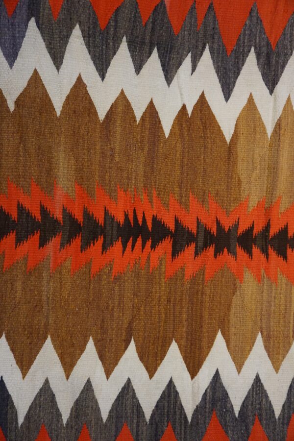 Coarse flatweave rug with brown, white, rust, and black zigzag and sawtooth patterns.
