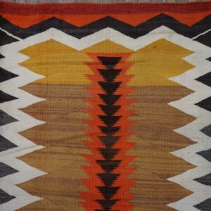 Low-pile rug with a central spine of dark triangles flanked by thick zigzags in orange, mustard, white, and black.
